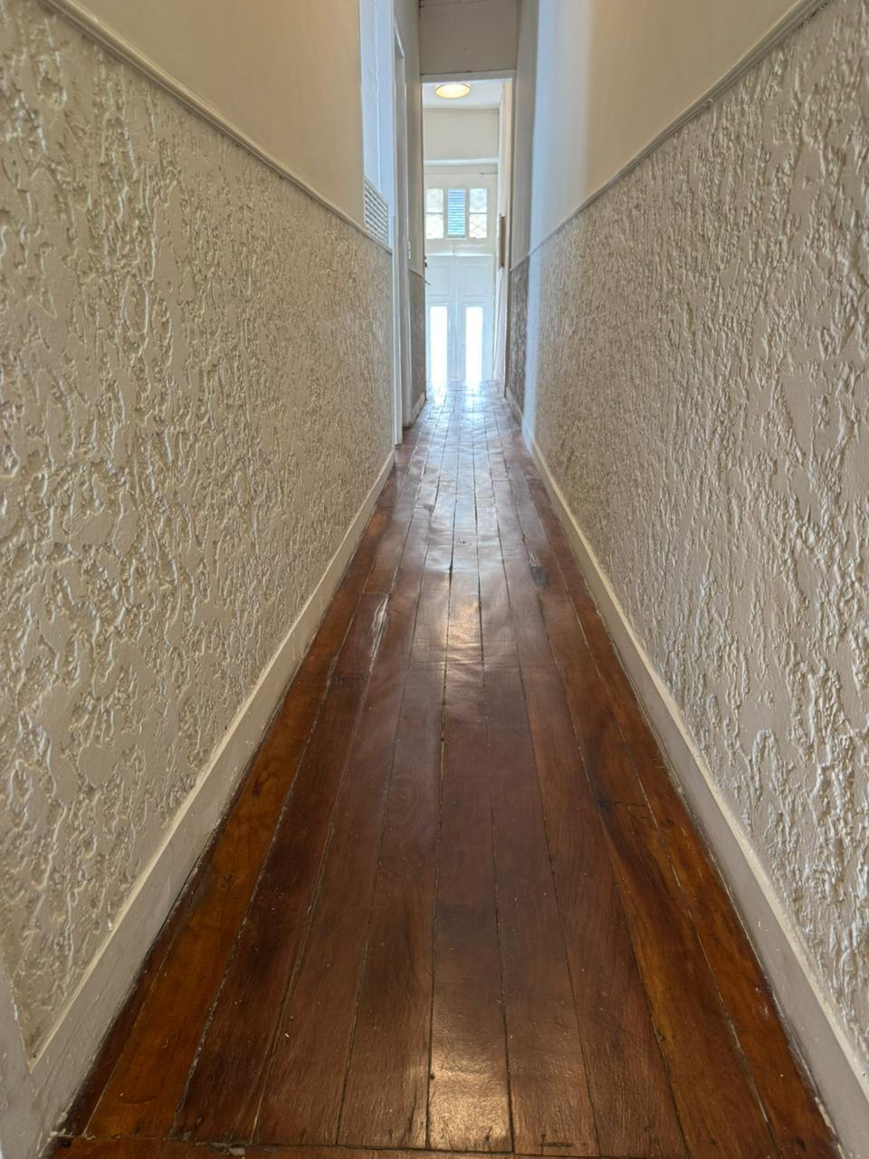 Corredor interno com piso de madeira até a entrada da casa