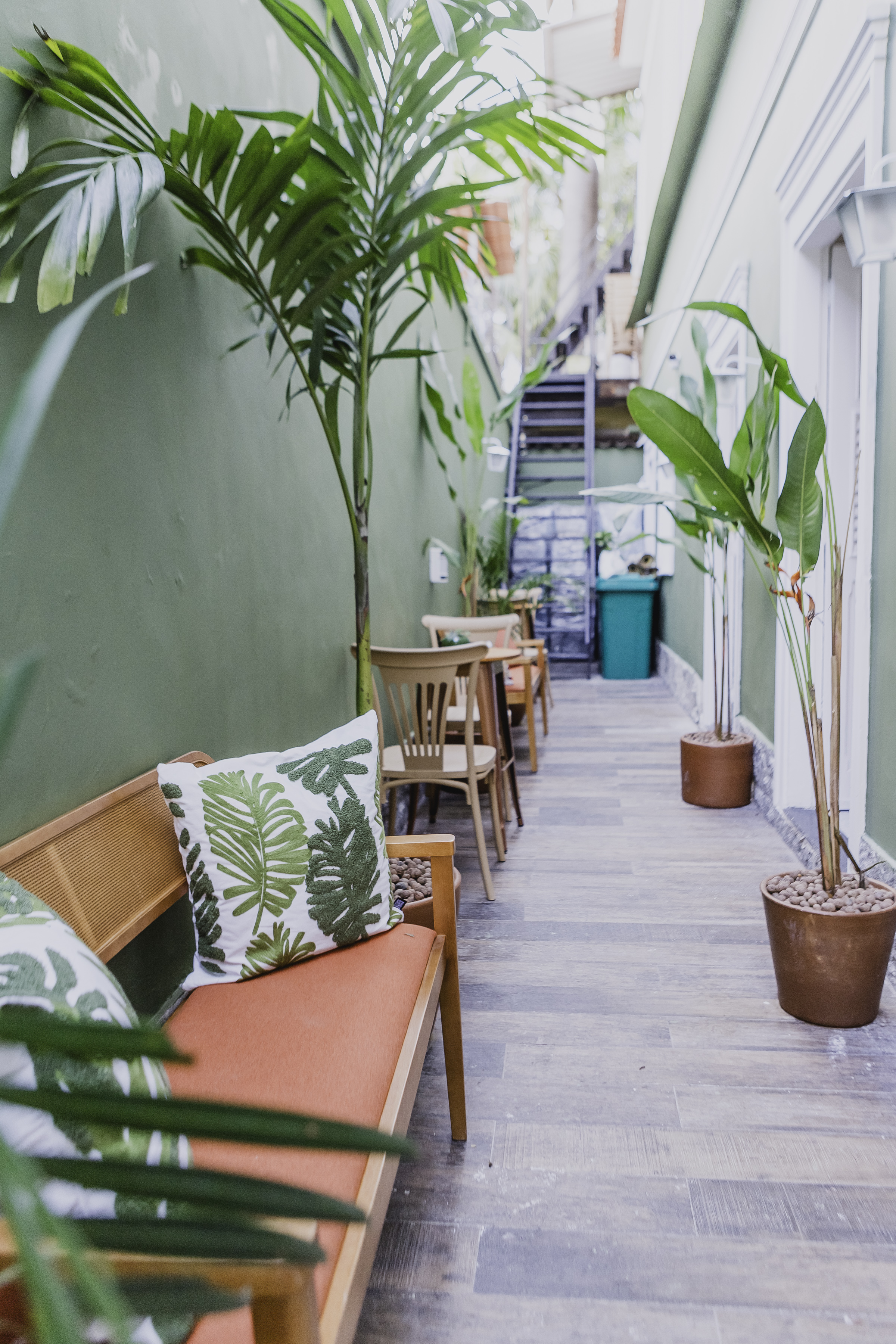 Corredor externo com bancos, cadeiras e plantas tropicais