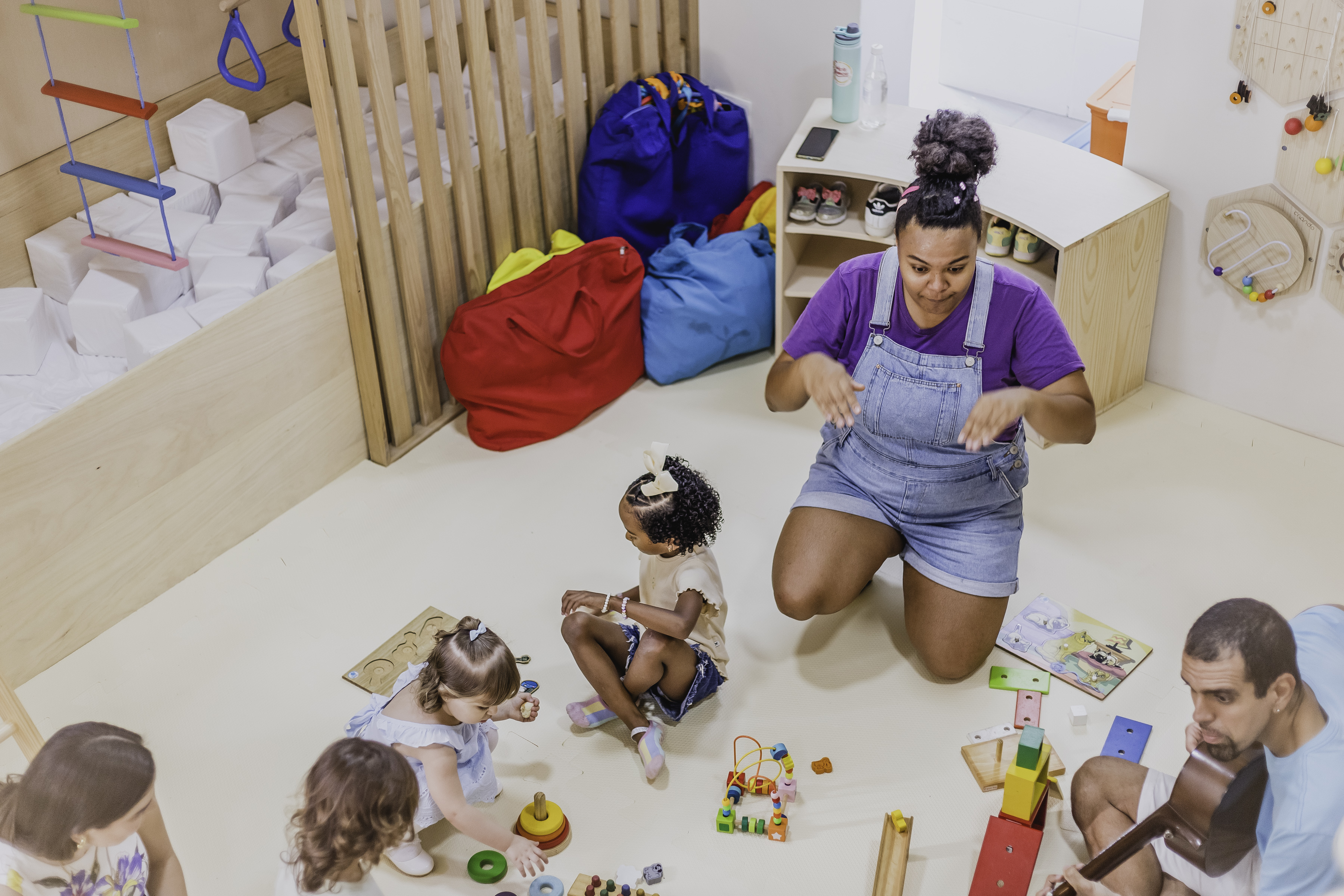 Monitora brincando com bebês e brinquedos de madeira no chão