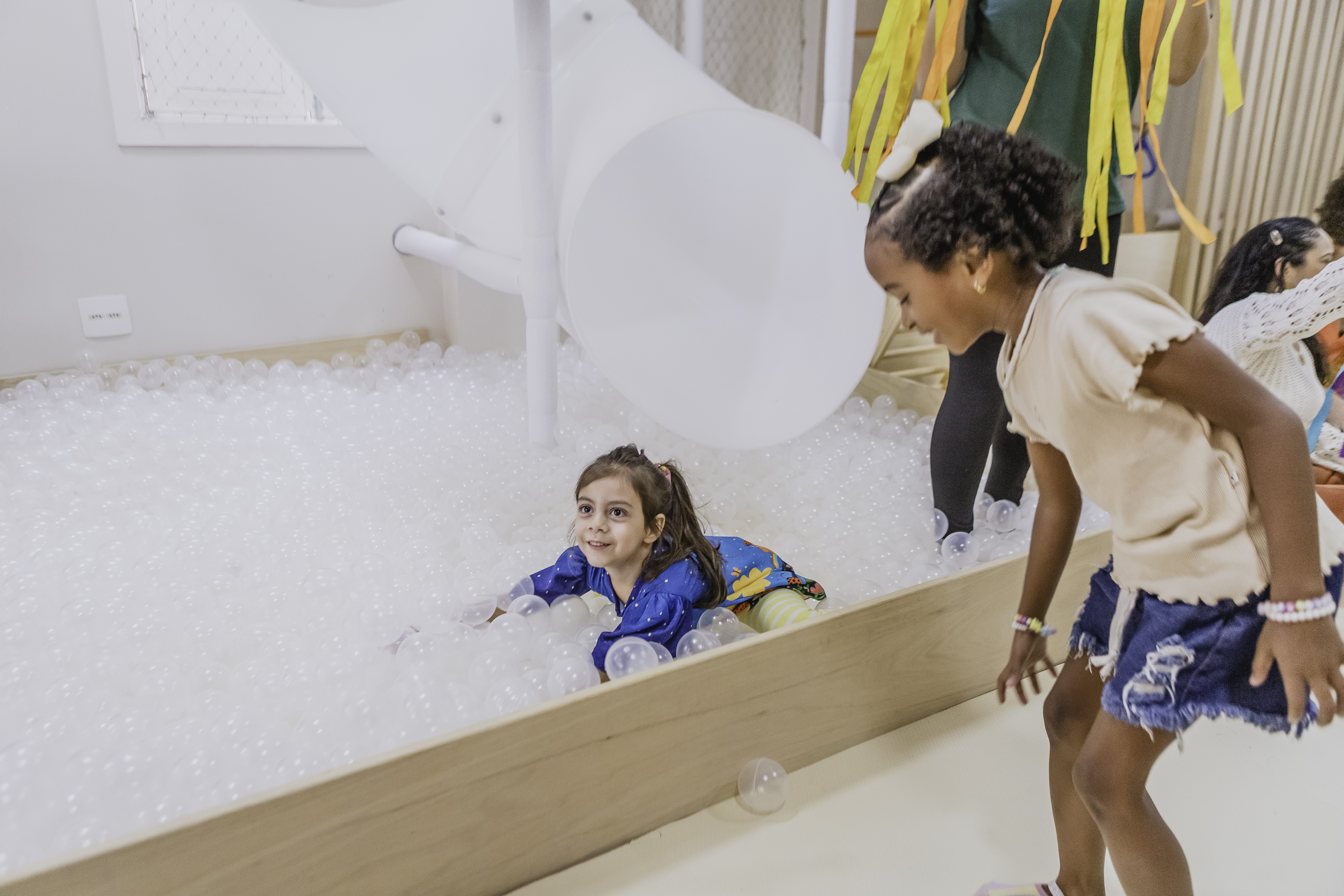 Criança na piscina de bolinhas com tobogã ao lado de outra menina