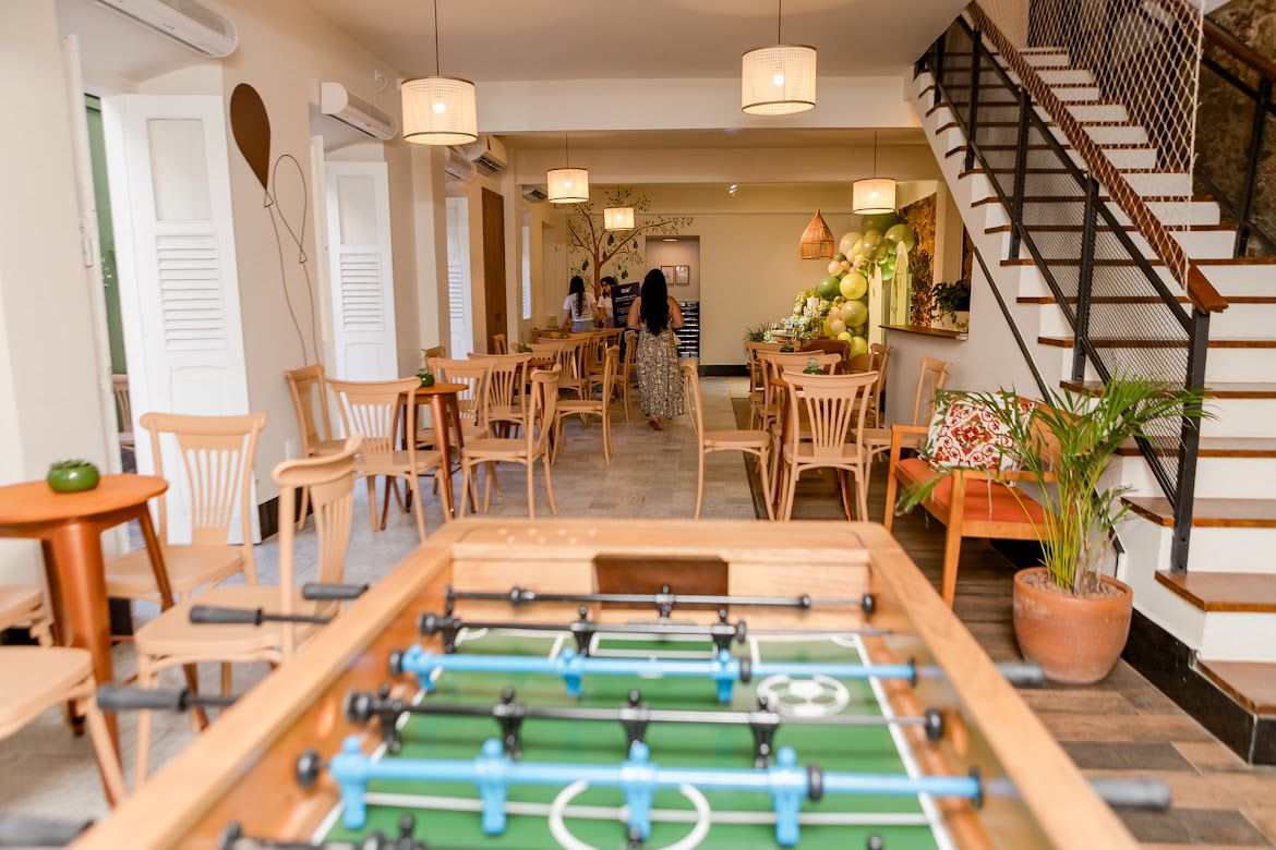 Salão com mesa de pebolim, plantas e escada de madeira ao fundo