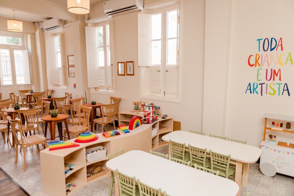Sala infantil com mesas verdes e frase Toda criança é um artista na parede