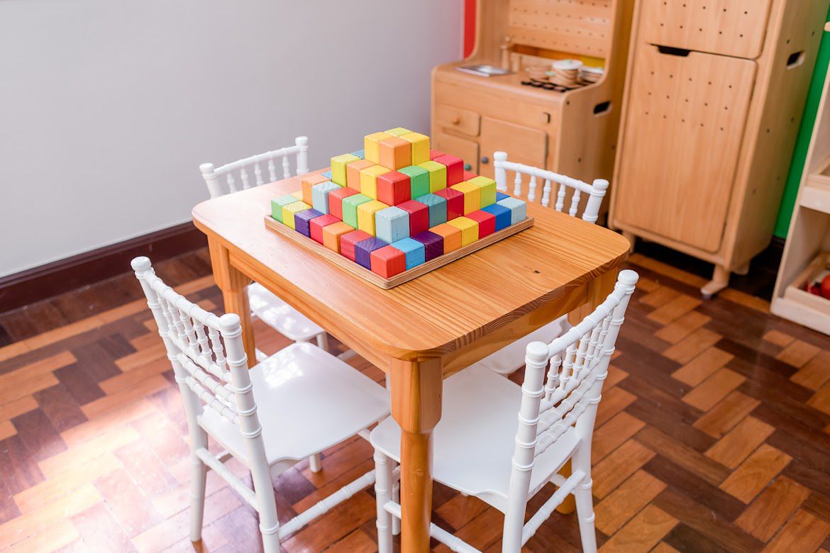 Mesa infantil com blocos de montar coloridos e cozinha de brinquedo ao fundo